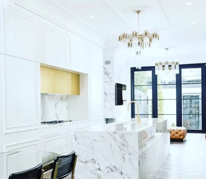 Kitchen with floor-to-ceiling panelled white cabinetry, brass-finish upper cabinets and a marble waterfall island