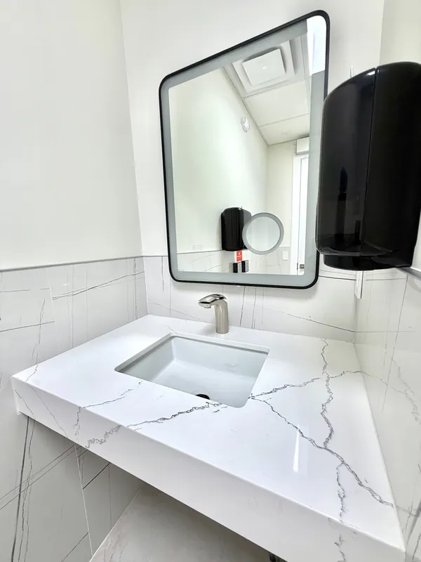 Floating quartz vanity with an undermount sink, porcelain wall tile and a backlit mirror